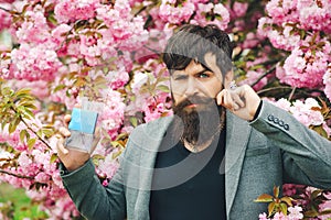 Masculine perfume. Spring flowers. Man perfume, fragrance. Male fragrance and perfumery, cosmetics. Man holding up bottle of