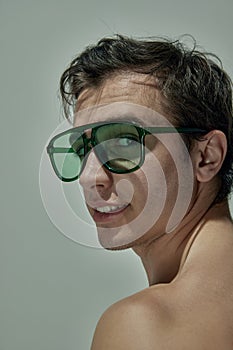 Masculinity. Portrait of handsome young man posing in green sunglasses over grey studio background. Concept of men& x27;s