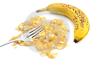 Mashed banana with fork and an unpeeled fruit