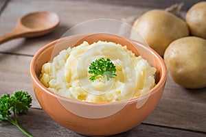 Mashed potato in bowl and fresh potatoes on table