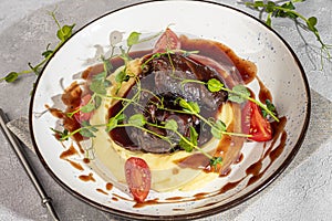 Mashed potatoes with beef in sweet and sour sauce, decorated with tomatoes and microgreens.