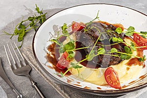 Mashed potatoes with beef in sweet and sour sauce, decorated with tomatoes and microgreens.