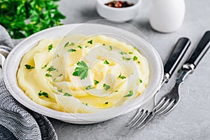 Mashed Potatoes with butter and fresh parsley in a white bowl on gray stone background