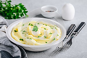 Mashed Potatoes with butter and fresh parsley in a white bowl on gray stone background