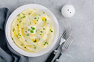 Mashed Potatoes with butter and fresh parsley in a white bowl on gray stone concrete background