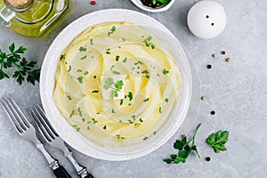 Mashed Potatoes with butter and fresh parsley in a white bowl on gray stone concrete background