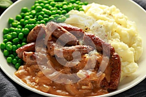 Mashed potatoes and sausages, bangers with onions gravy, green peas. close up