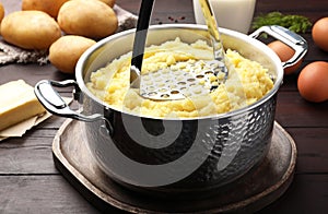 Mashing potatoes in pot on wooden table, closeup