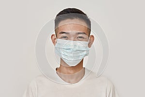 Mask on. Portrait of young asian man wearing medical mask, smiling at camera  over white background. Health care