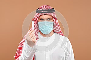 A masked Arab man holds a test tube in a national costume on a beige background