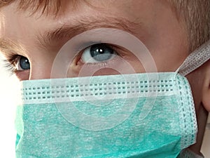 Masked child. The face of a 7-year-old boy in a protective surgical mask close-up. Schoolboy with blond hair and blue-gray eyes on