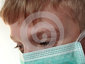 Masked child. The face of a 7-year-old boy in a protective surgical mask close-up. Schoolboy with blond hair and blue-gray eyes on