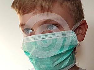 Masked child. The face of a 7-year-old boy in a protective surgical mask close-up. Schoolboy with blond hair and blue-gray eyes on