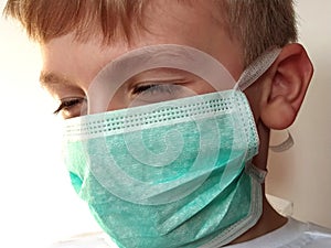 Masked child. The face of a 7-year-old boy in a protective surgical mask close-up. Schoolboy with blond hair and blue-gray eyes on