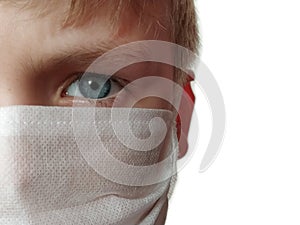 Masked child. The face of a 7-year-old boy in a protective white surgical mask close-up. Schoolboy with blond hair