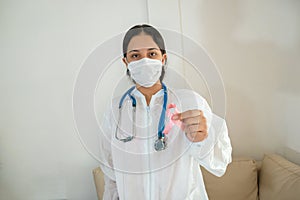 Masked doctor holds a pink ribbon for breast cancer awareness