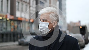 Masked gentleman with graying hair in black coat and shirt walks on city streets