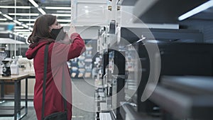 Masked girl picks out new microwave oven in electronics shop