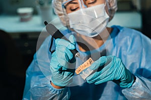 A masked and gloved dental technician works on a prosthetic tooth in his lab