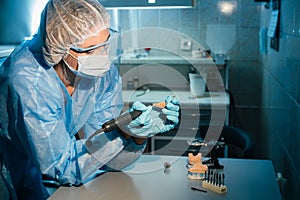 A masked and gloved dental technician works on a prosthetic tooth in his lab