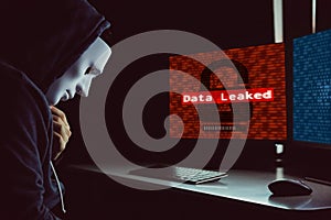 Masked hacker under hood using computer to hack into system and employ data leaking process