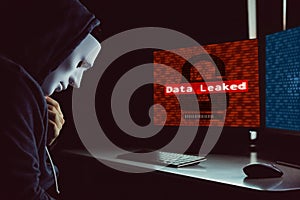 Masked hacker under hood using computer to hack into system and employ data leaking process photo