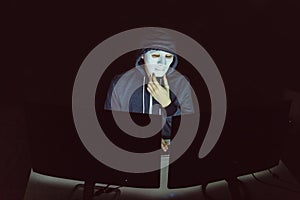 Masked hacker under hood using computer to hack into system and trying to commit computer crime.