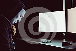 Masked hacker under hood using computer to hack into system and trying to commit computer crime.