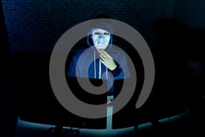 Masked hacker under hood using computer to hack into system and trying to commit computer crime.
