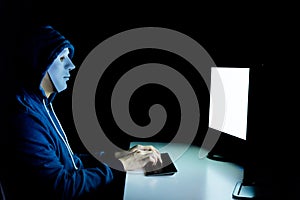 Masked hacker under hood using computer to hack into system and trying to commit computer crime.