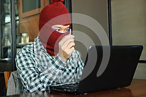 Masked hacker wearing a balaclava holding fake key between stealing data from laptop. Internet crime concept.