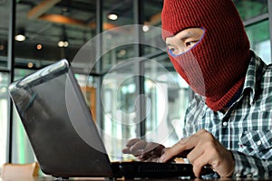 Masked hacker wearing a balaclava looking a laptop and stealing important information data. Network security and privacy crime con