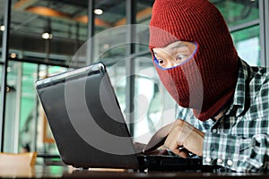 Masked hacker wearing a balaclava stealing data from laptop. Internet crime concept.