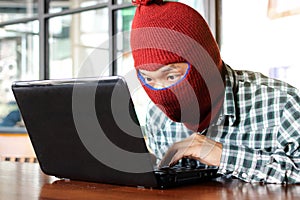 Masked hacker wearing a balaclava stealing importance data from laptop. Internet crime concept.