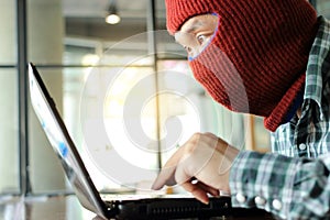 Masked hacker wearing a balaclava stealing importance data from laptop. Internet crime concept.