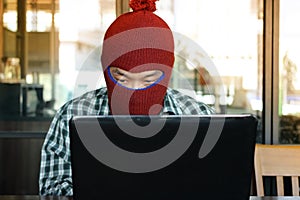 Masked hacker wearing a balaclava stealing information data with laptop. Computer criminal concept.