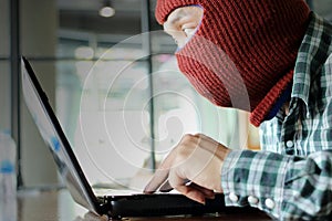 Masked hacker wearing a balaclava using laptop stealing important information data. Internet security and privacy crime concept. S