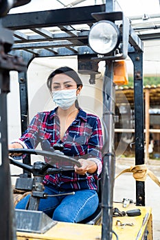 Masked hispanic woman sits behind the wheel of a tractor autocar during a pandemic.