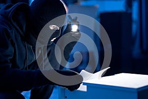 Masked intruder holding and reading confidential documents