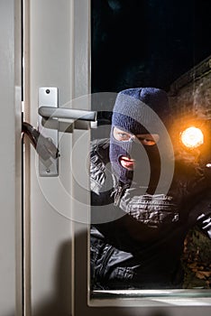 Masked intruder holding torch while trying to open window with c