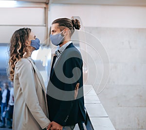 Masked man and woman in love stand at a subway station.