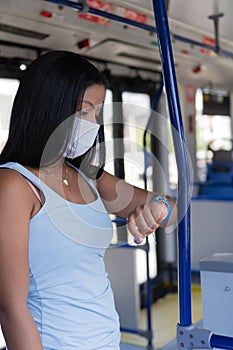 Masked passenger standing in the aisle and checking the time while traveling on a bus in the middle of a pandemic