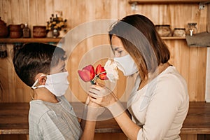 A masked son gives flowers to a masked mom. Mother`s Day on self-isolation. Family quarantined