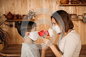 A masked son gives flowers to a masked mom. Mother`s Day on self-isolation. Family quarantined