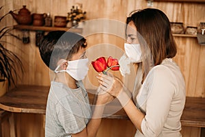 A masked son gives flowers to a masked mom. Mother`s Day on self-isolation. Family quarantined