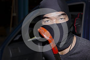 Masked thief with balaclava holding crowbar to breaking into a car. Crime concept