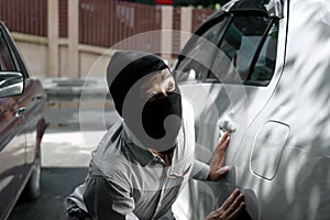 Masked thief in black balaclava trying to break into car. Criminal crime concept