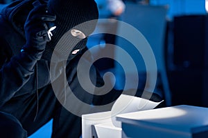 Masked thief holding and reading confidential documents