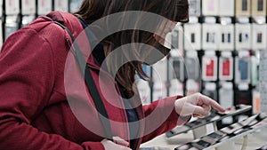 Masked woman buys a tablet from a modern electronics store