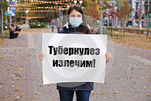 A masked woman holds a poster with text in Russian, translated from Russian - Tuberculosis is curable photo